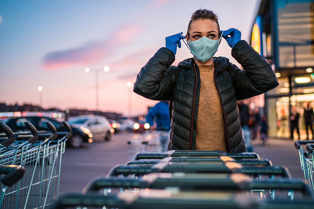 AdobeStock 332517690 Eine junge Frau setzt sich vor einem Einkaufszentrum eine Maske auf